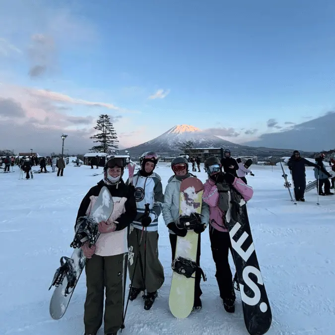 Group of 4 friends carrying snowboards in front of Mount Yotei