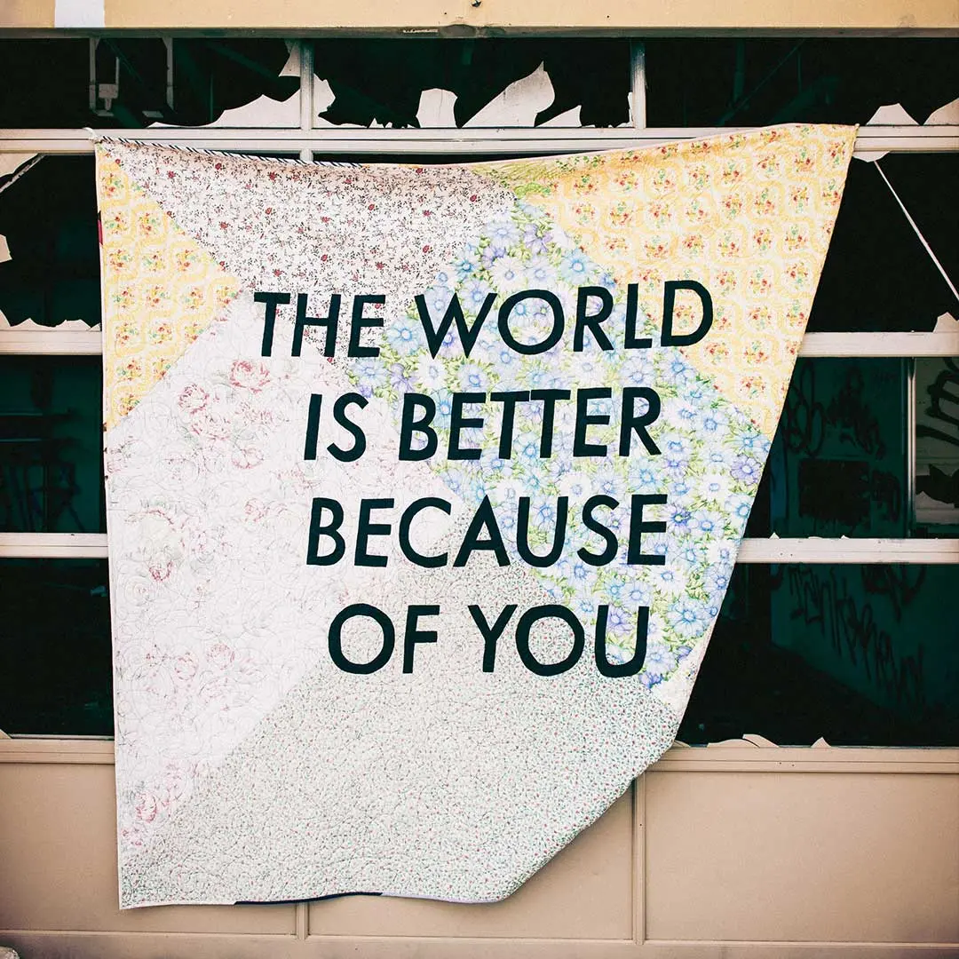 The words 'The world is better because of you' are on a sheet hanging out a window - From Tim Mossholder via Unsplash