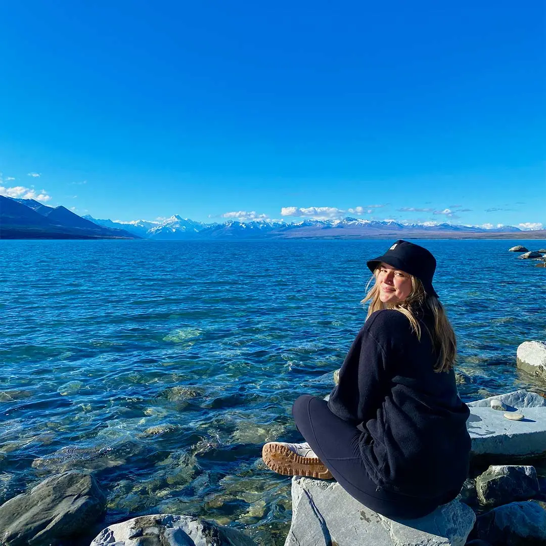 Girl looks back on edge of blue lake on sunny day.