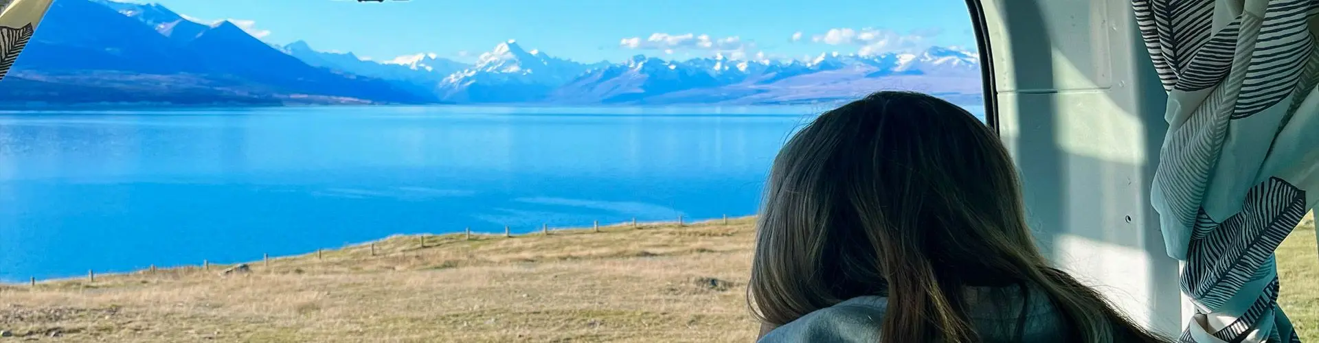 Girl looks out back of van at lake