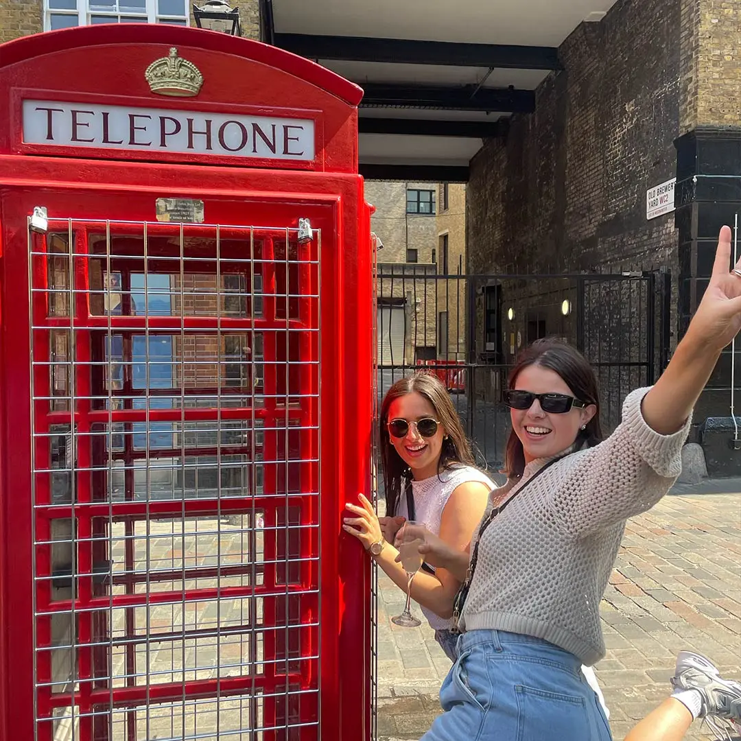 Two girls posing beside red phone box in London