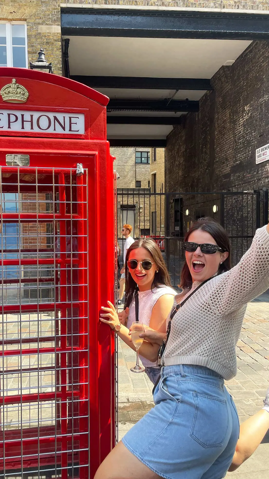 2 girls pose beside English red telephone box