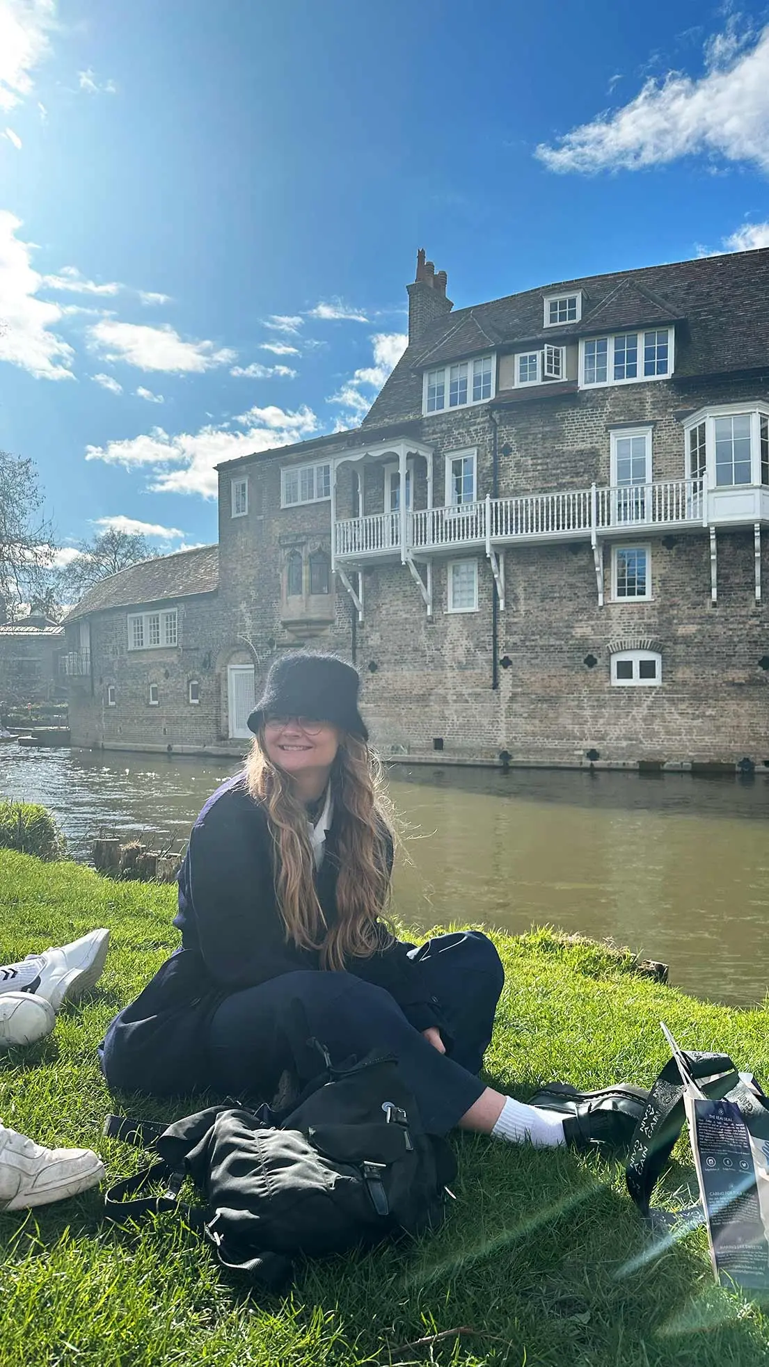 Girl sits beside stream and old english house