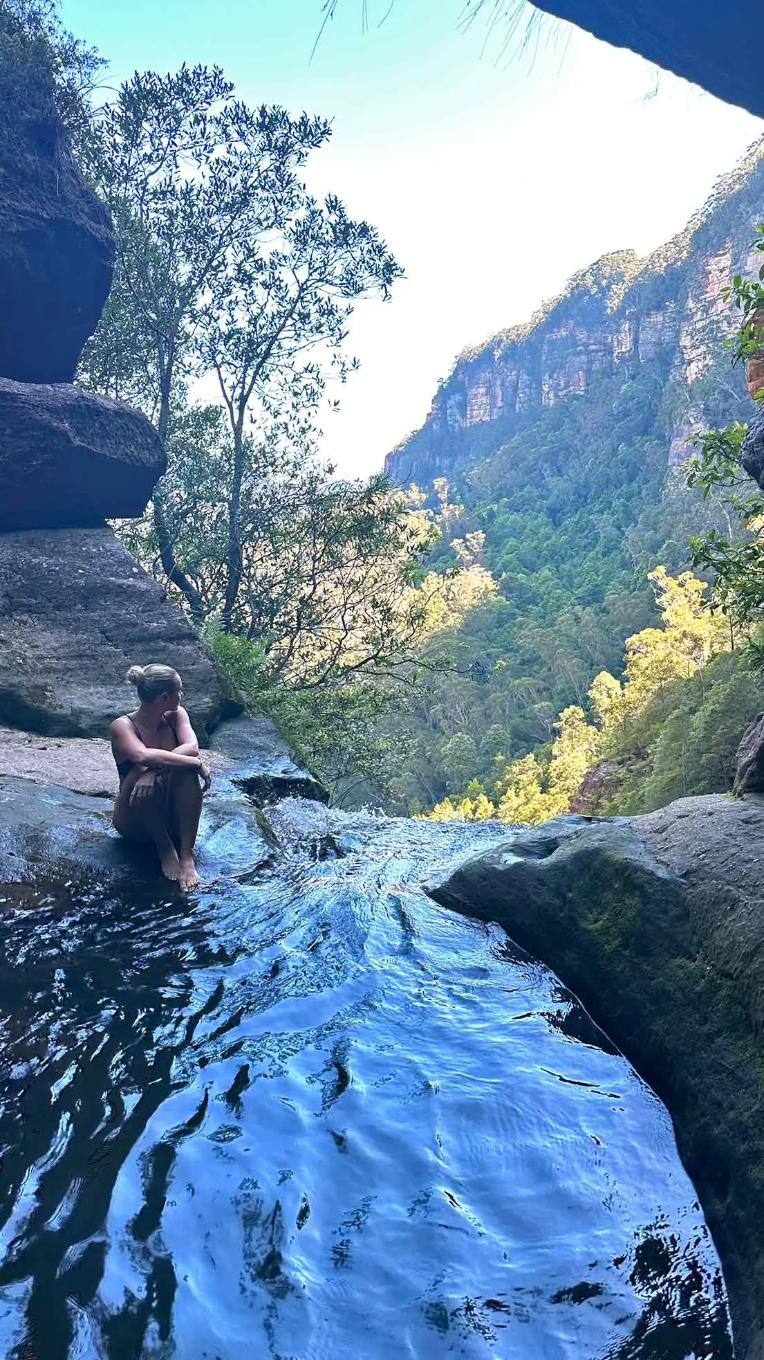 Girl sits beside cave waterfall