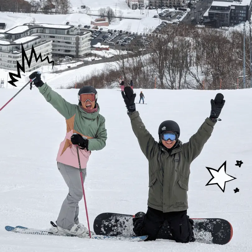 Two skiiers in Japan holding up their arms on snowy slopes