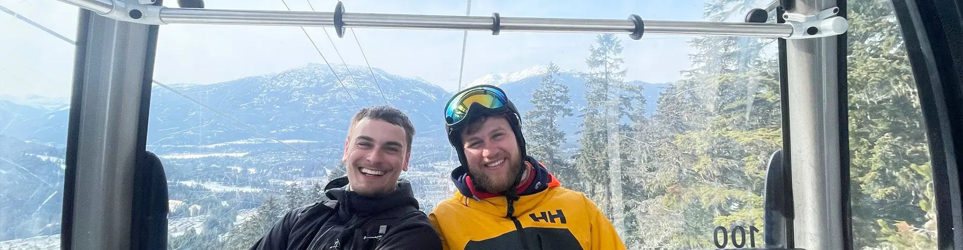 2 guys on ski lift smile with mountains in background