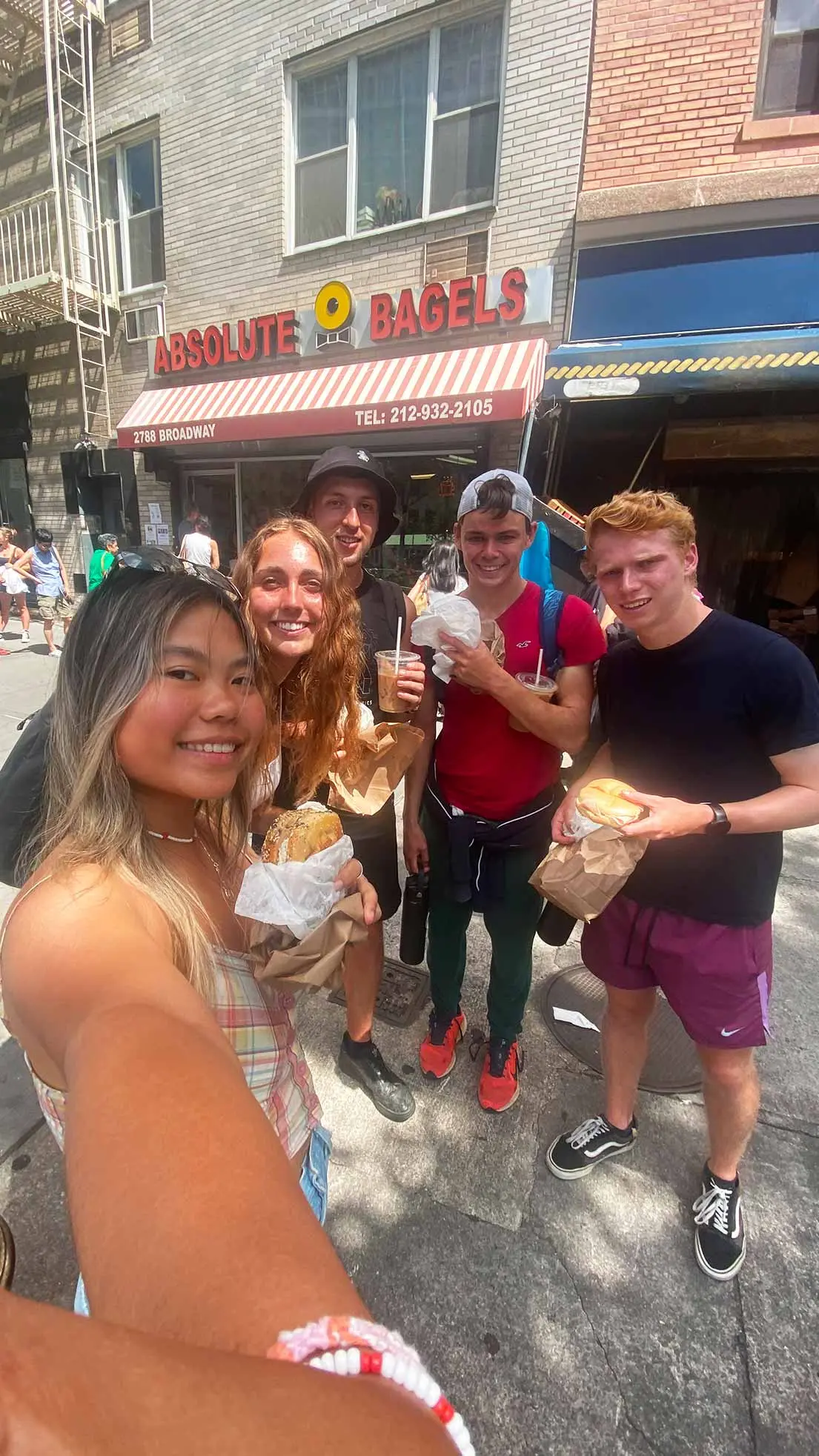 Group of friends take selfie outside bagel shop.