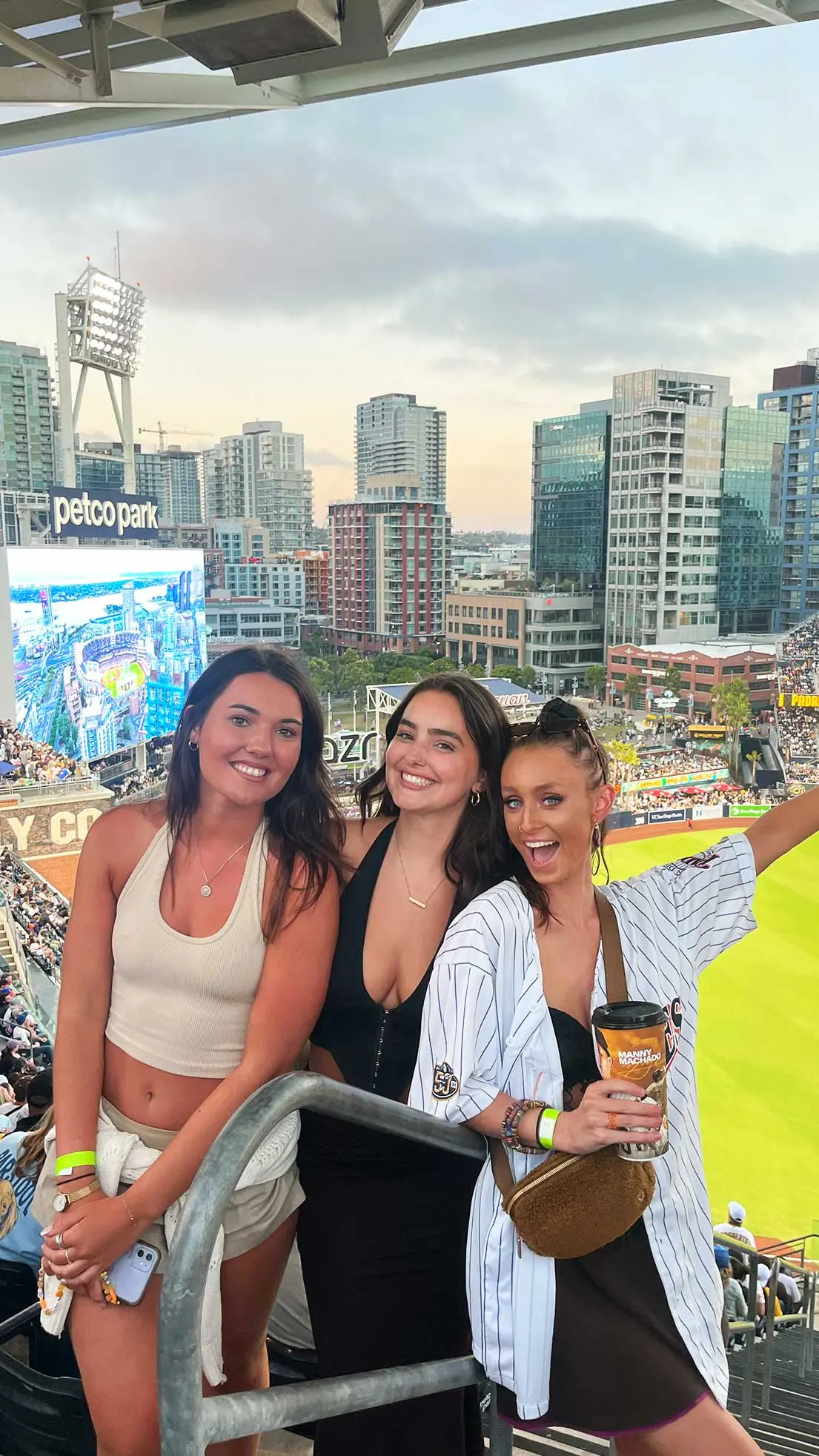 Three girls at baseball match pose for photo.