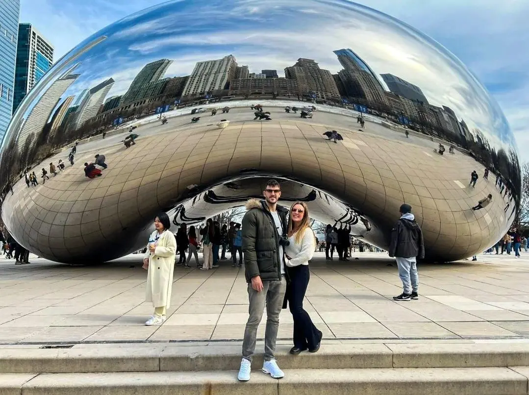 A young couple stand in front of the Bean in Chicago during the day