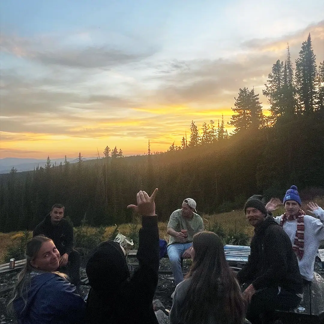 Friends sit around a fire at sunset in the woods