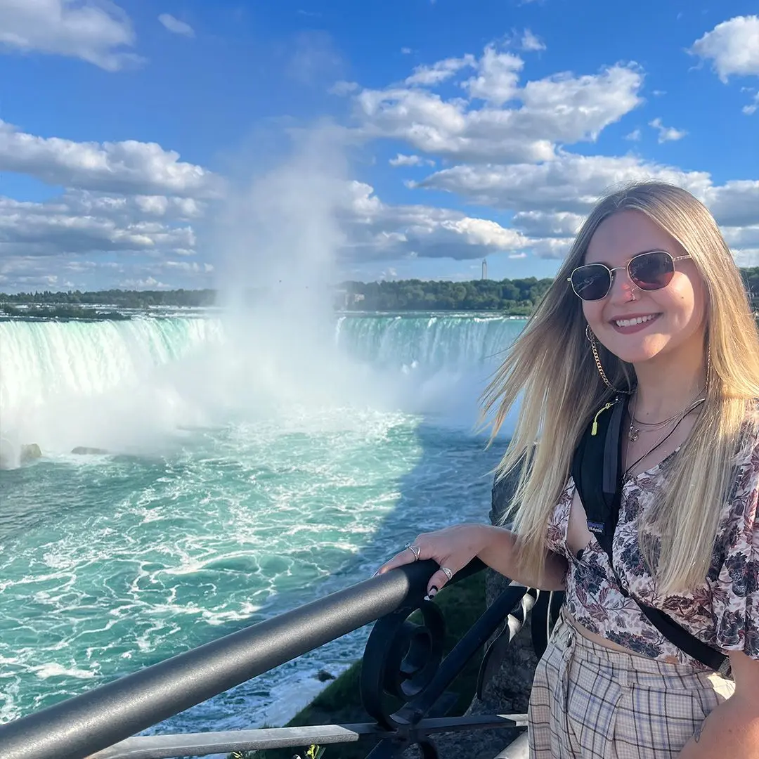 Girl with sunglasses smiles at camera in front of big waterfall