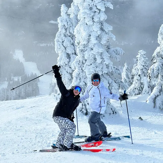 Friends smile for photo on ski slope with white tree in background