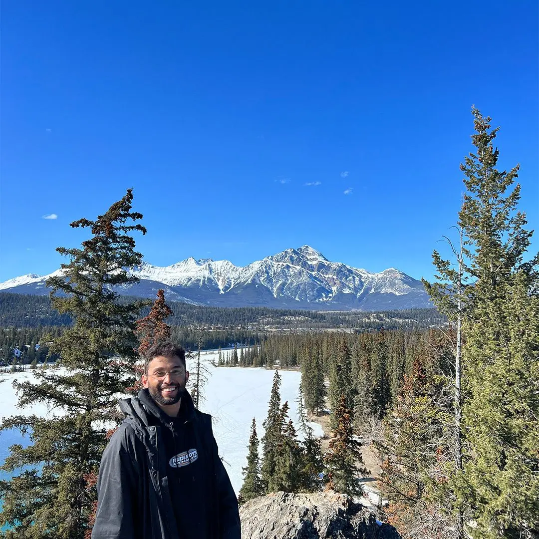 guy smiles at camera in front of mountains on sunny day