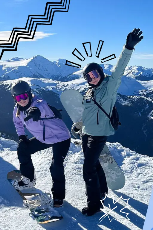 Two girls skiing on top of a mountain in the sun