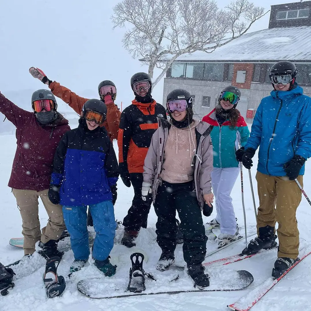 A group of skiiers and snowboarders stand in the snow and smile at the camera